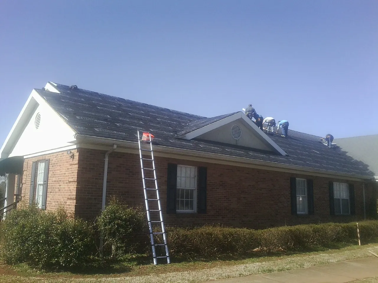 Crew tearing shingles off a brick ranch roof with a ladder set — Emergency Roof Repair work by our crew in Far Hills