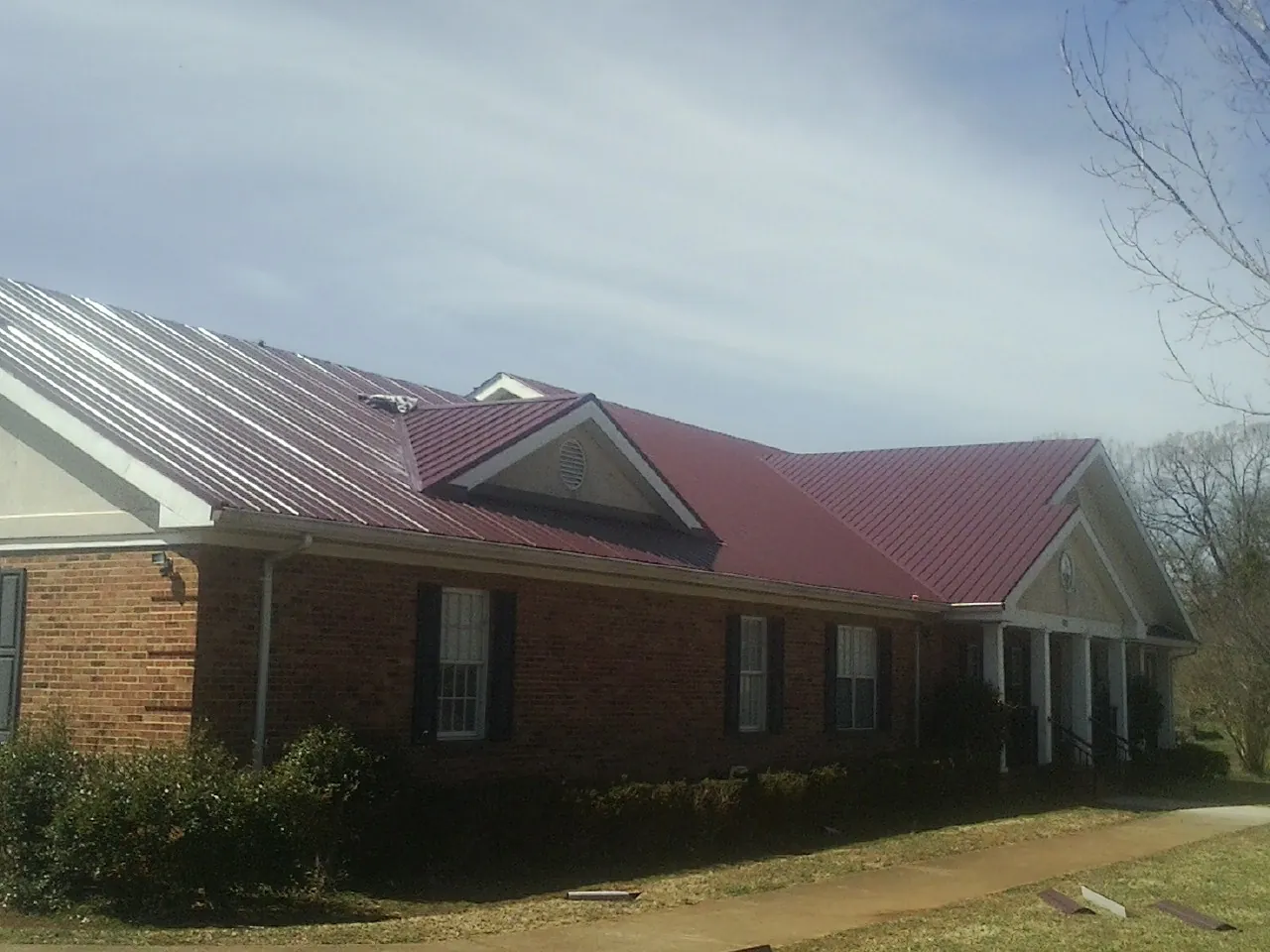 Red metal roof with gabled entries on a long brick building, from a Hail Damage Roof Repair job in Far Hills