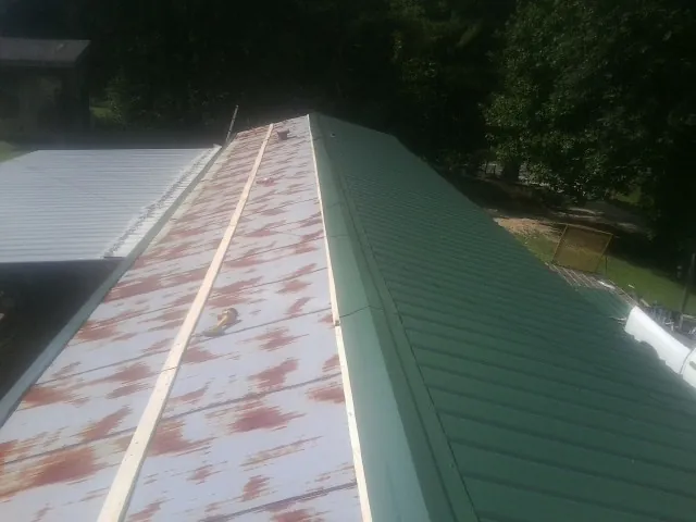 Old rusted panels beside newly installed green metal roofing — Wind Damage Roof Repair by Roofing Brothers in Far Hills