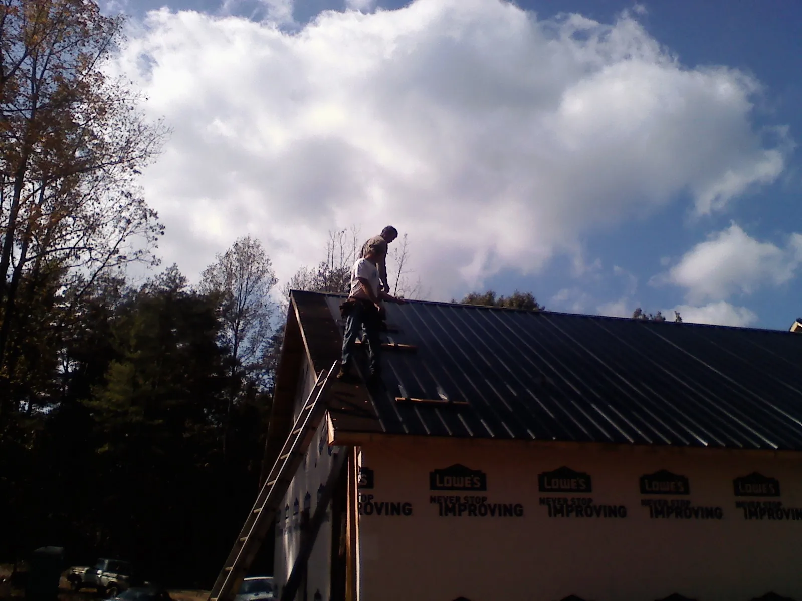 Roofer fastening dark metal panels high against a cloudy sky, from a Roof Inspection job in Far Hills