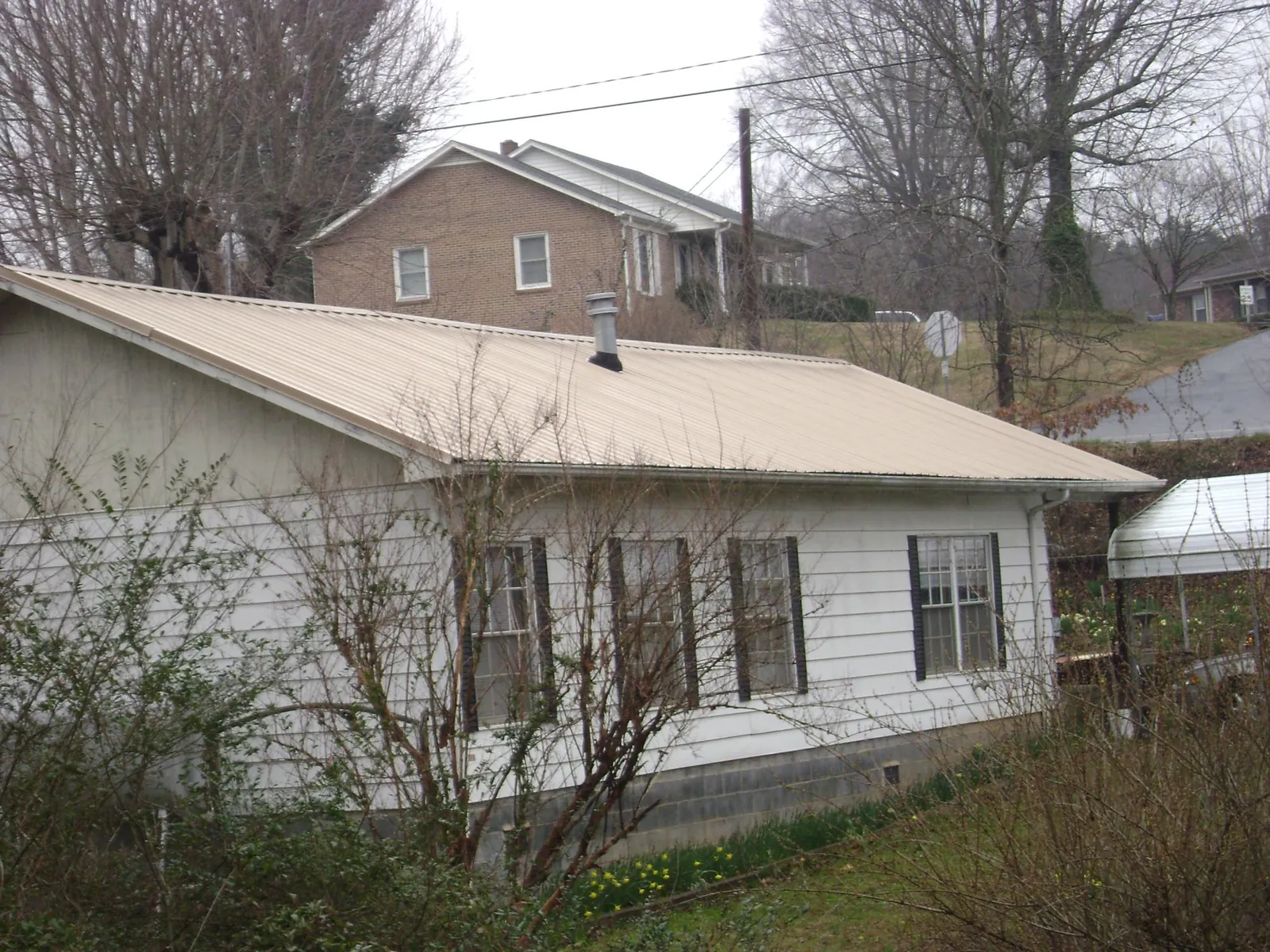 Tan metal roof on a white sided house set into a hillside — Commercial Roofing by Roofing Brothers in Far Hills